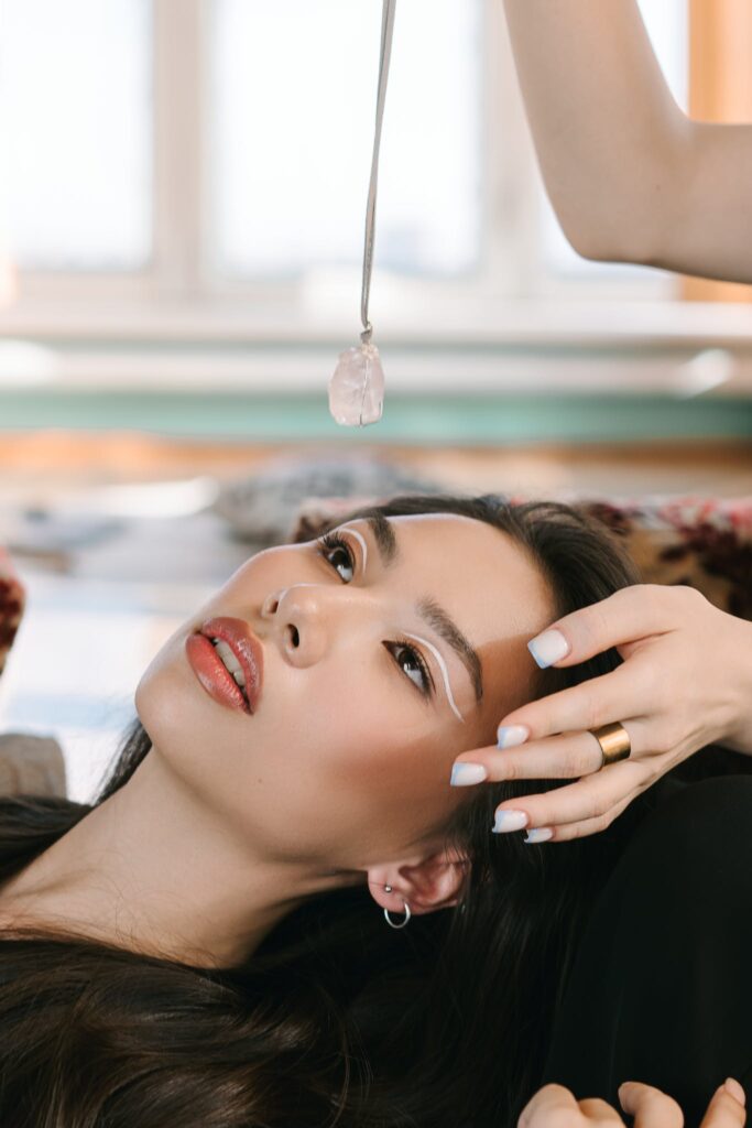 High angle of ethnic female client with stylish makeup lying under pendulum during alternative medicine session